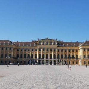 Frontansicht vom Schloss Schönbrunn vor blauem Himmel, davor ein Platz mit einigen Menschen